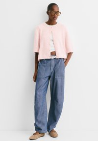 Cardigan rose clair à manches courtes avec une texture douce, fermeture à boutons ; associé à un pantalon cargo ample à rayures verticales bleues et des mocassins marron.