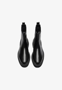 Bottes en cuir noir montantes avec une finition lisse, des panneaux latéraux élastiques et des tirettes. Elles présentent une semelle épaisse et texturée avec un détail de couture.