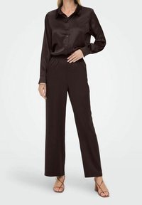 Femme portant un chemisier en satin marron foncé à manches longues et un pantalon large assorti avec des talons à lanières beiges.