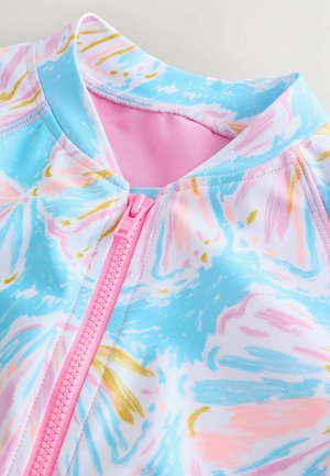 Lähikuva värikkäästä vetoketjullisesta vaatetuksesta, jossa on vaaleanpunainen vetoketju ja abstrakteja pastellinsävyisiä korallin, sinisen, valkoisen ja kullan kuvioita kankaassa.