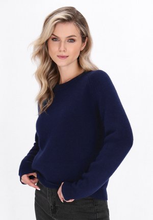 Granatowy sweter wykonany z miękkiego materiału, z okrągłym dekoltem, długimi rękawami i prążkowanymi mankietami oraz dołem. Noszony z czarnymi dżinsami.