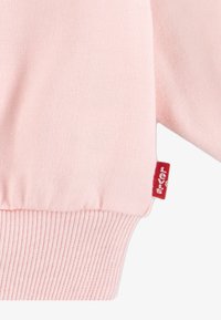 Svetlo roza pulover s rebrastim manšeto, s majhnim rdečim Levi's oznako na strani. Mehka tekstura tkanine, preprost dizajn.