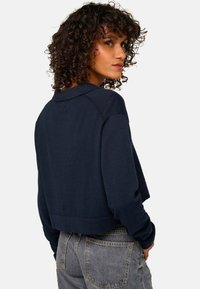 Pull cropped bleu marine avec col, bord à côtes et manches longues, fabriqué dans un tissu doux au toucher lisse.