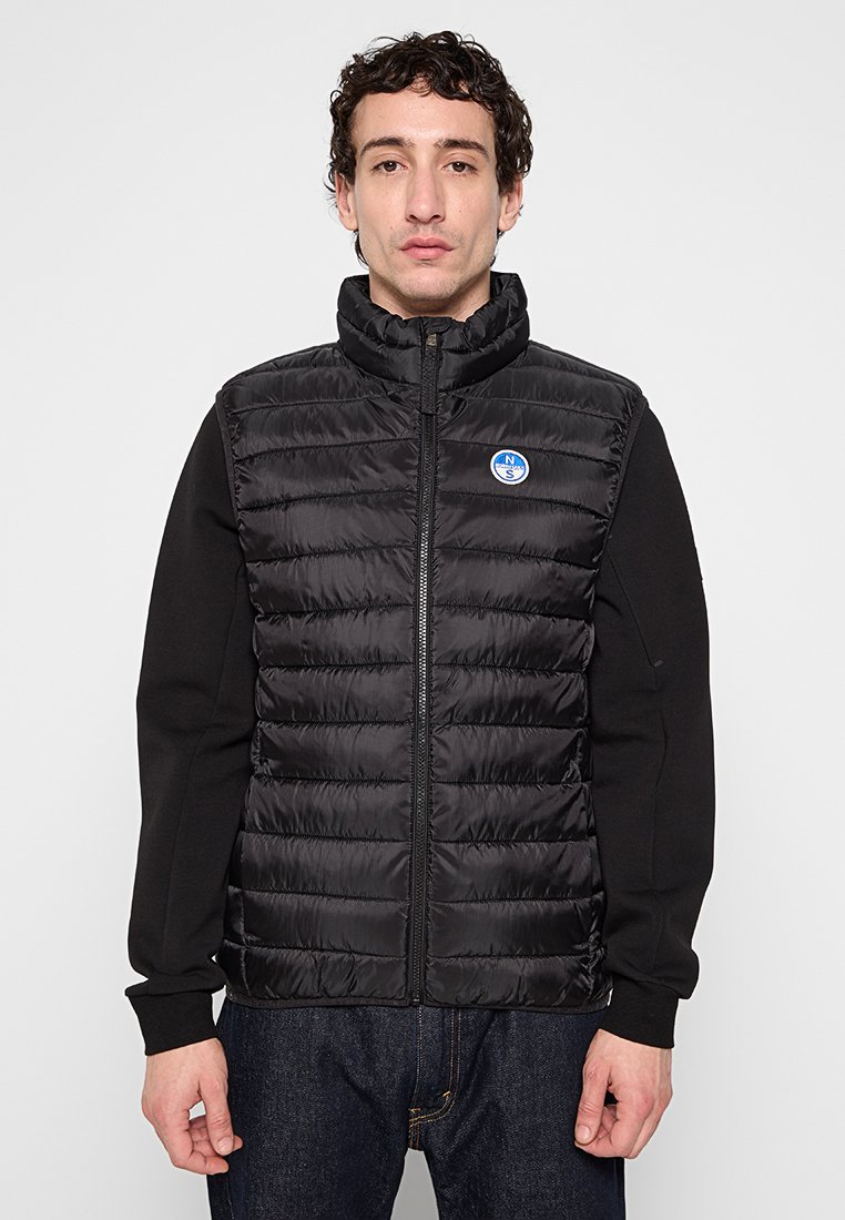 Gilet imbottito nero con colletto alto, chiusura a zip e motivo trapuntato orizzontale. Presenta un logo circolare blu sul lato sinistro.