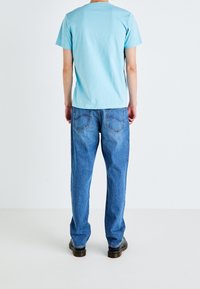 Ljusblå bomullst-shirt och löst sittande blå denimjeans. T-shirten har rundad krage, jeansen har bakfickor med sömdetaljer.