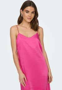 Vestito in raso rosa con spalline sottili, scollo a V e una texture liscia, che arriva appena sopra le ginocchia. Design semplice, senza motivi.