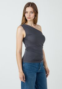 Grau einseitiges Oberteil mit weichem, dehnbarem Material, enganliegendem Schnitt und gerafftem Detail an der Taille, kombiniert mit blauen High-Waisted-Jeans.