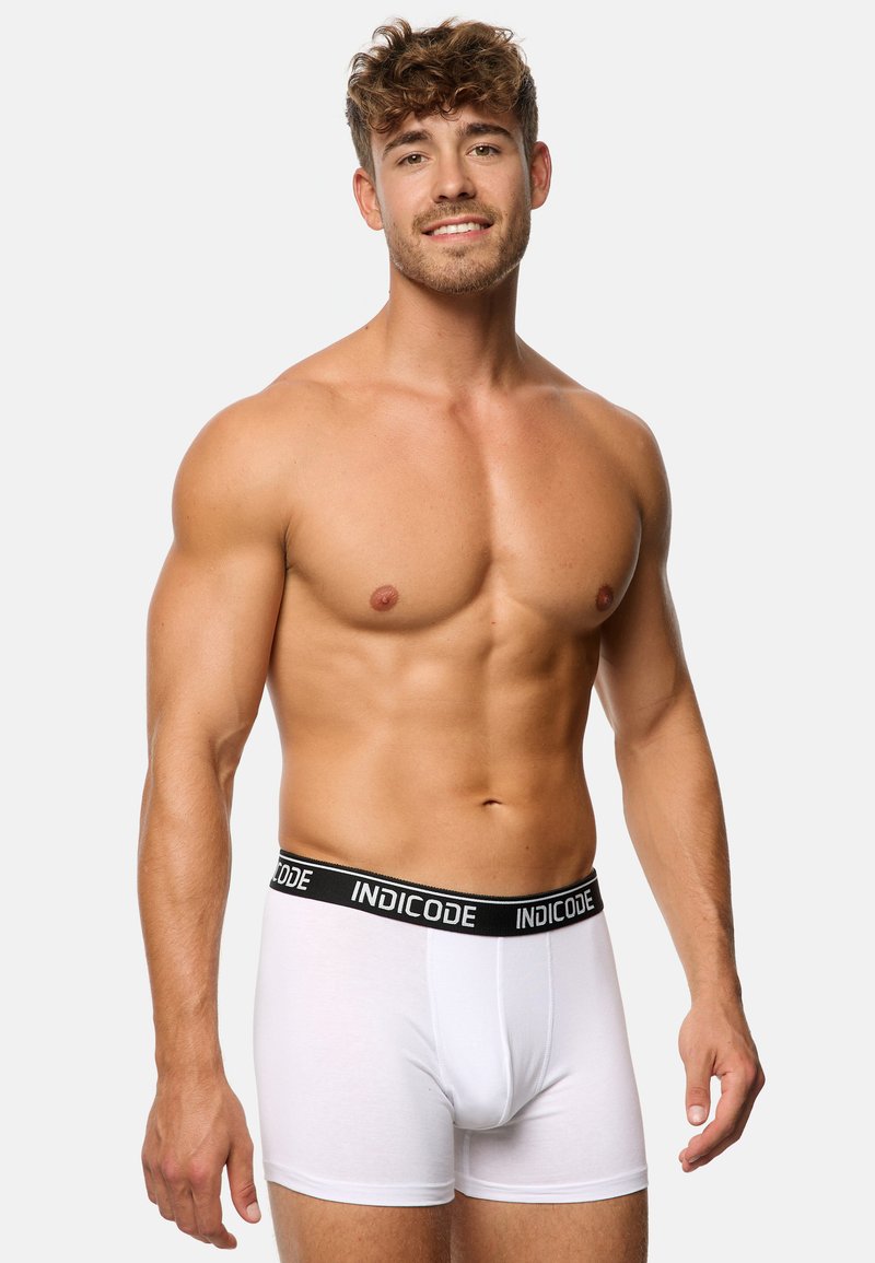 Hvide bomulds boxer briefs med en sort talje, der har "INDICODE" tekst. Glat tekstur, tætsiddende design og klassisk form.