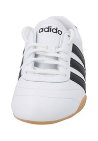 Vit sportskor med svart tre-stripesdesign, rund tå, gummisula och vita snören. Varumärkeslogotypen är synlig på tungan.