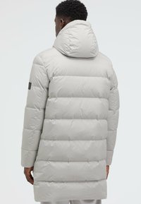 Light gray puffer coat with a detachable hood, featuring a quilted design and a black logo patch on the left sleeve. Smooth texture.
