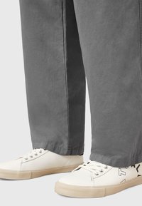 Pantalons larges gris au toucher lisse associés à des baskets blanches avec des accents noirs et des semelles crème texturées.