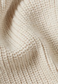 Tessuto a maglia beige con una texture a costine. Il filato è spesso, mostrando un aspetto morbido e accogliente con un motivo a boucle costante.