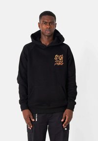 Sudadera negra con un bolsillo tipo canguro en la parte frontal, capucha ajustable con cordón y gráfico de llamas naranjas en el pecho. Tejido suave, corte relajado.