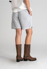 Gray mesh shorts with side pockets and contrasting white trim paired with knee-high brown leather boots featuring a side zipper and buckle.