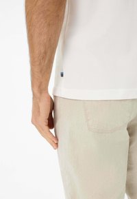Hvid polo-shirt med en syet kant, parret med lyse beige bukser. Bemærkelsesværdige detaljer inkluderer en lille farvet accent ved skjortens side søm.