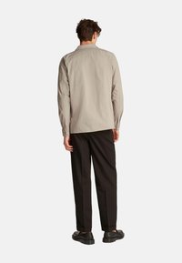 Camisa de manga larga gris claro con cuello tipo polo, yugo trasero y puños abotonados, combinada con pantalones negros y zapatos negros.