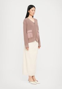 Svetlo mauve cardigan z rebrastim vzorom, dvema ravnima sprednjima žepoma in zadrgo. V kombinaciji z dolgo off-white krilo in belimi mule. 