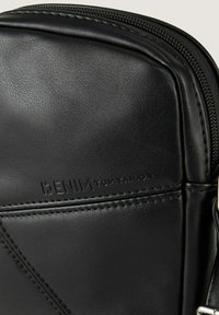 Borsa in pelle nera con superficie testurizzata, dotata di chiusura a zip e logo in rilievo. Include dettagli di cucitura e un accento metallico.