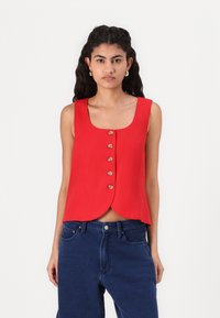 Red sleeveless top with a rounded hem, featuring six front buttons. Made of a smooth fabric, paired with high-waisted blue jeans.