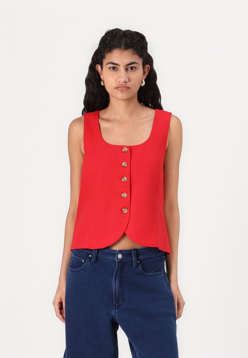Red sleeveless top with a rounded hem, featuring six front buttons. Made of a smooth fabric, paired with high-waisted blue jeans.