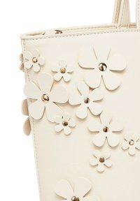 Bílá taška přes rameno s 3D květinovými aplikacemi a zlatými nýty. Vyrobena z texturované syntetické kůže, disponuje dvojitými ramenními popruhy a pevnou strukturou.