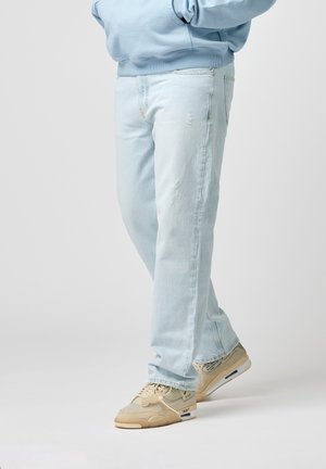 Lichtblauwe denim jeans met een ontspannen pasvorm, voorzien van versleten details en traditionele zakken. Gepaard met beige sportsneakers.