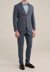 Traje azul marino de rayas finas con una silueta ajustada, hecho de tela texturizada, combinado con una camisa de botones azul clara y mocasines negros.