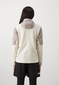 Φλις μπουφάν σε ανοιχτό κρέμ με γκρι επενδυμένα ώμους και κουκούλα. Διαθέτει ελαστικές λεπτομέρειες και ευθεία γραμμή στο ύψος της μέσης. Συνδυάζεται με μαύρες σορτς.