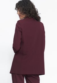 Burgundowa dopasowana marynarka z długimi rękawami, kołnierzem i lekko wydłużonym krojem. Gładki materiał i minimalistyczny design.