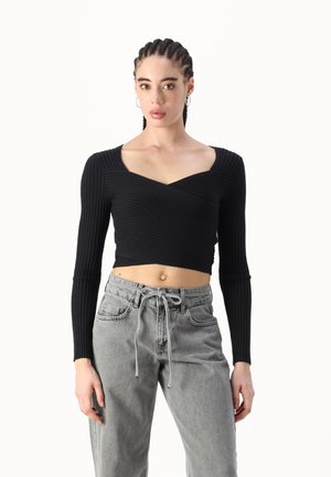 Black ribbed long-sleeve crop top featuring a square neckline and twisted front design, paired with high-waisted grey denim pants.