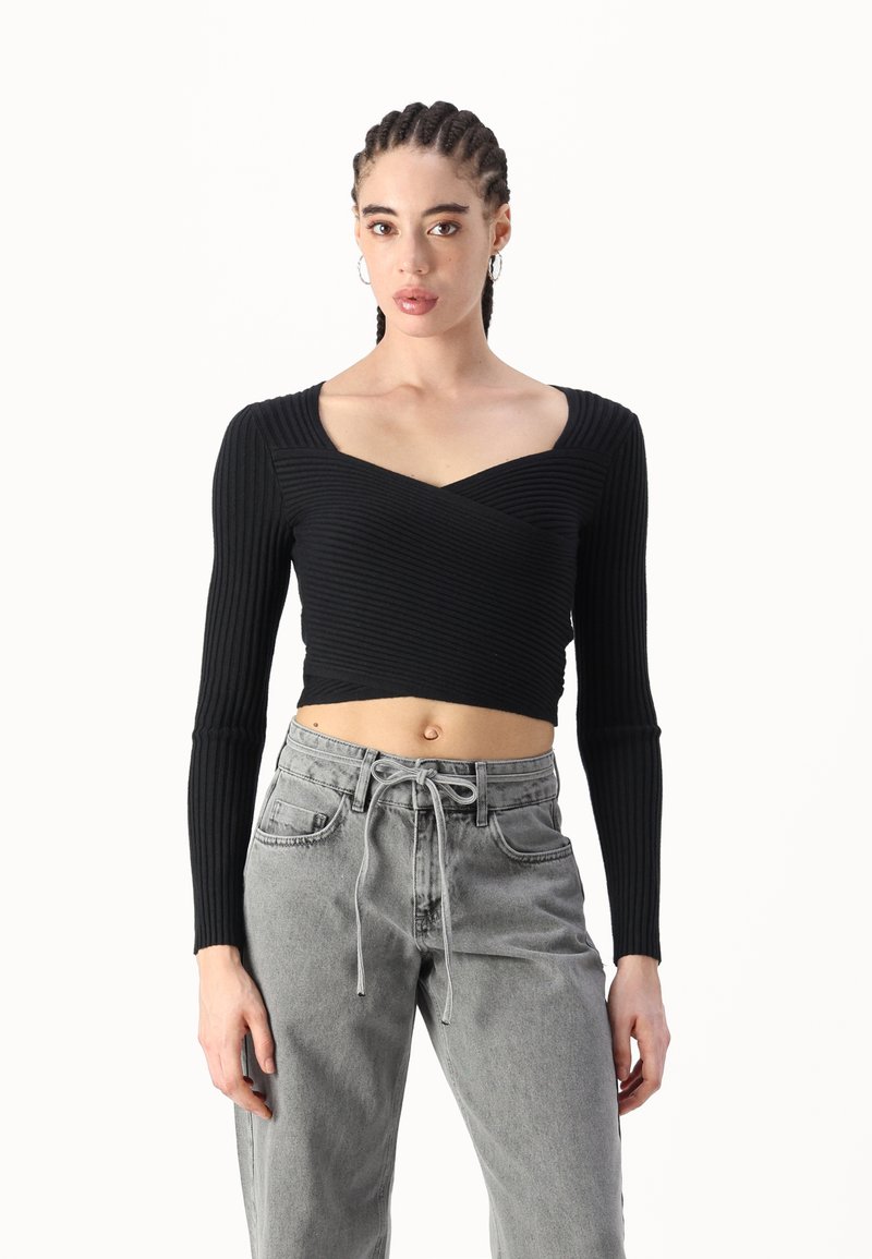 Top corto de manga larga negro de canalé con escote cuadrado y diseño delantero retorcido, combinado con pantalones de mezclilla gris de cintura alta.