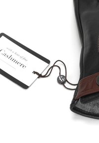 Svart läderhandske med brunt läderdetalj, försedda med en etikett som säger "med en aning fin kashmir" och en mörk rund knappfäste.