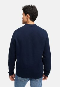 Marineblaues Langarm-Polohemd mit strukturierter Oberfläche, ausgestattet mit einem klassischen Kragen, gerippten Manschetten und einem geraden Saum. Tragen Sie es mit hellblauen Jeans.