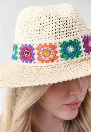 Woman wearing a cream crochet sunhat with a colorful crocheted band featuring green, purple, orange, and blue floral square patterns.