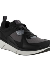 Czarny but sportowy z siateczkową cholewką, gładkimi syntetycznymi akcentami, grubą białą podeszwą i kontrastującymi teksturowanymi wzorami.