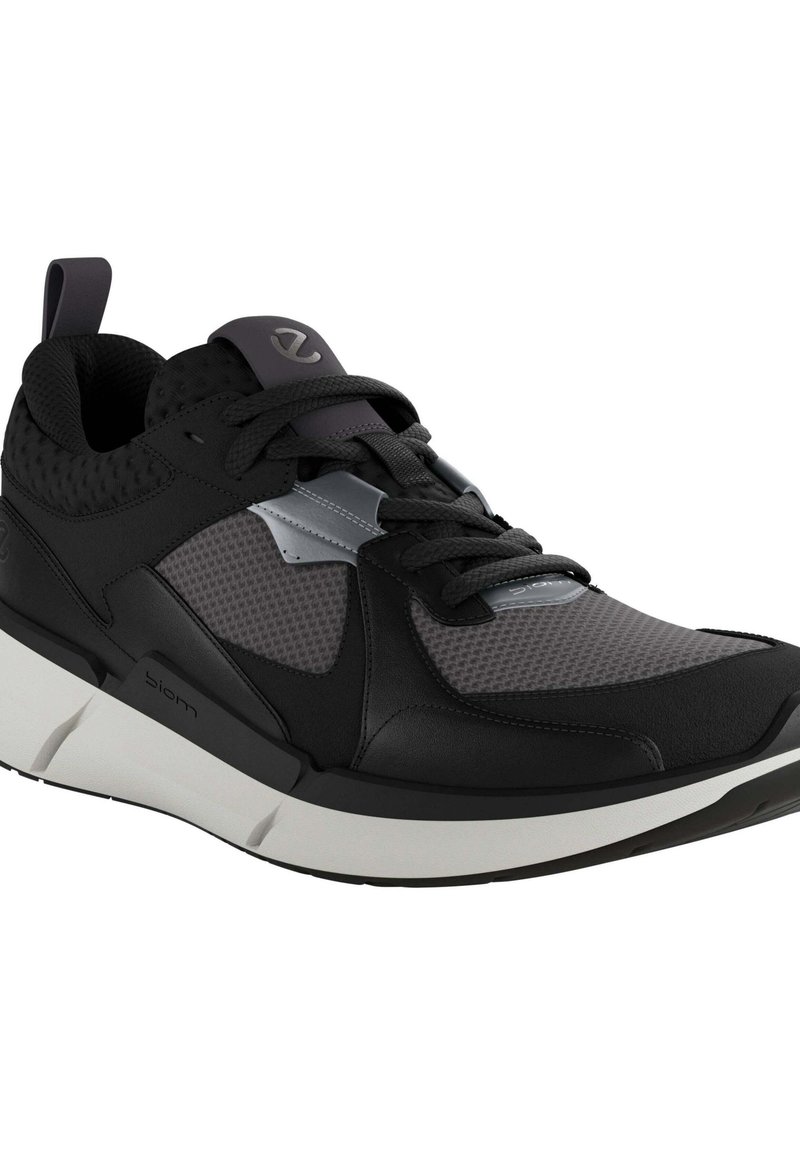 Schwarzer Sportschuh mit einem Obermaterial aus Mesh, glatten synthetischen Akzenten, einer dicken weißen Sohle und kontrastierenden strukturierten Mustern.