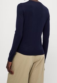Maglione a manica lunga in maglia di colore blu navy con scollo a girocollo, vestibilità aderente e orlo a coste. Il modello indossa dei pantaloni beige.