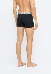 Černé boxerky vyrobené z měkké tkaniny s šedým elastickým pasem s logem "NIKE". Design zahrnuje těsné padnutí a středně dlouhé nohavice.