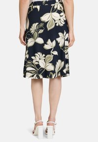 Marineblumenkleid mit cremefarbenen und olivgrünen Blumen, elastischem Taillenbund, knielang, glattes Material, kombiniert mit weißen Blockabsatzsandalen.