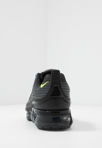 Czarne buty sportowe z teksturowanym, prążkowanym wzorem na cholewce, z neonowożółtym akcentem i półprzezroczystą podeszwą powietrzną.