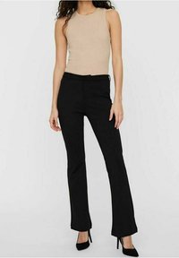 Débardeur beige ajusté, pantalon noir sur mesure légèrement évasé à l'ourlet, associé à des escarpins noirs. Texture lisse, sans motifs.