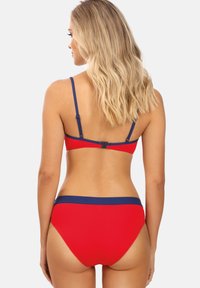 Czerwony zestaw bikini z niebieskimi wykończeniami, z cienkimi, regulowanymi ramiączkami. Góra ma zapięcie z tyłu, a dół ma wysoką talię.