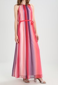 Robe maxi dans des tons de rose, violet et rouge. Dotée d'un col halter, d'un tissu fluide et d'une taille nouée. Matériau léger et transparent.