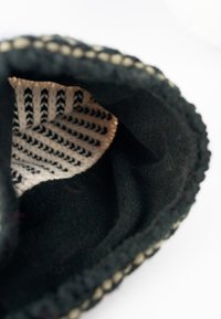 Black fleece slipper with a soft interior, featuring a patterned textile lining in white and black, and contrasting stitching along the edge.