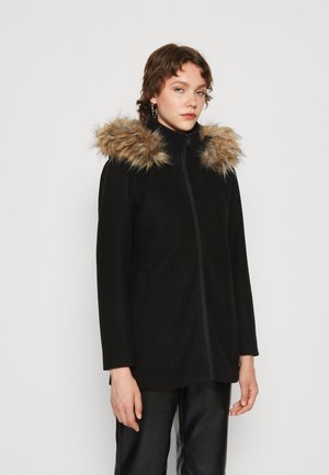 Veste noire avec fermeture éclair à l'avant et capuche doublée en fourrure. Présente des manches longues et des poches latérales. Le matériau a une texture douce et lisse.