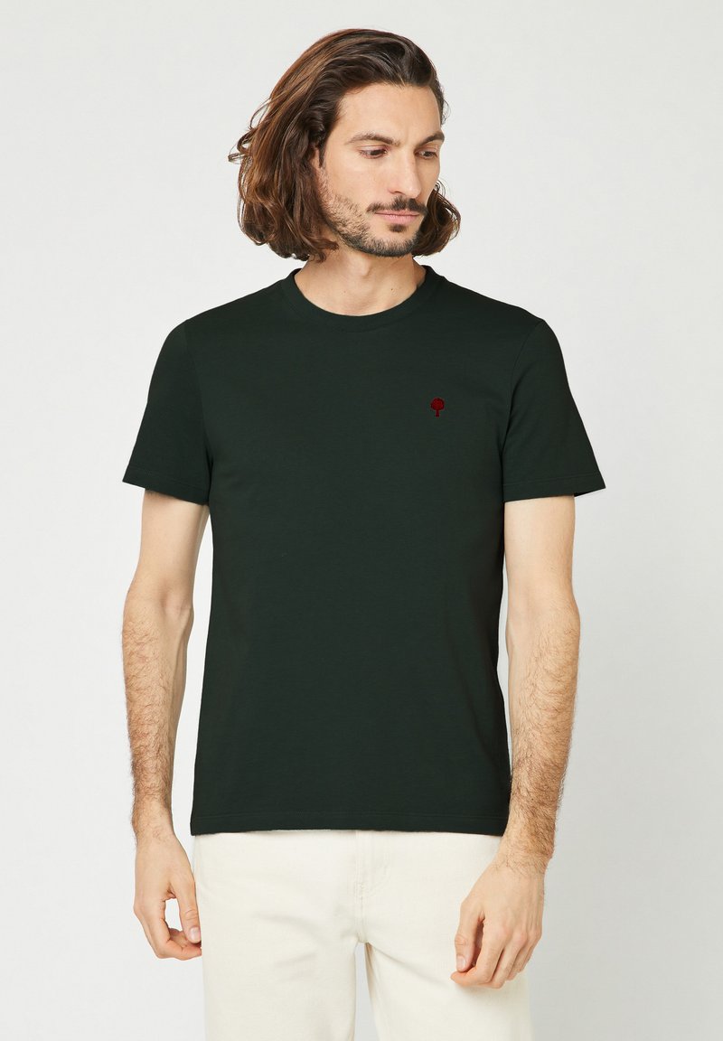 Donkergroene katoenen T-shirt met een klassieke ronde hals, korte mouwen en een klein rood boomsymbool op de linkerkant van de borst.