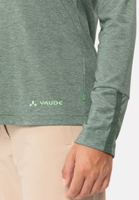 Grünes Langarmhemd aus strukturiertem Stoff mit einem subtilen melierten Muster. Mit markiertem Logo und Spitze an den Ärmelenden.