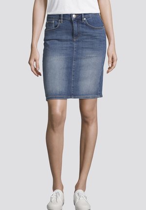 Jeansowa spódnica ołówkowa w średnim niebieskim kolorze z średnim stanem, kieszeniami z przodu i subtelnymi detalami w stichingu. Noszona z białymi trampkami.