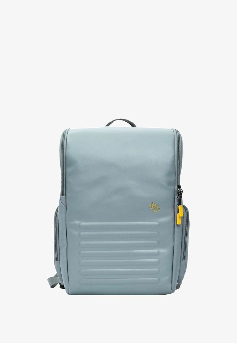 Mochila gris con un acabado liso, diseño estructurado, surcos verticales en la parte frontal y tirador de cremallera amarillo para un fácil manejo.