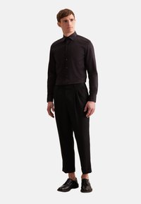 Zwarte overhemdbloes met kraag, gecombineerd met zwarte geplooide broek en zwarte veterschoenen. Glad materiaal en op maat gemaakt pasvorm.